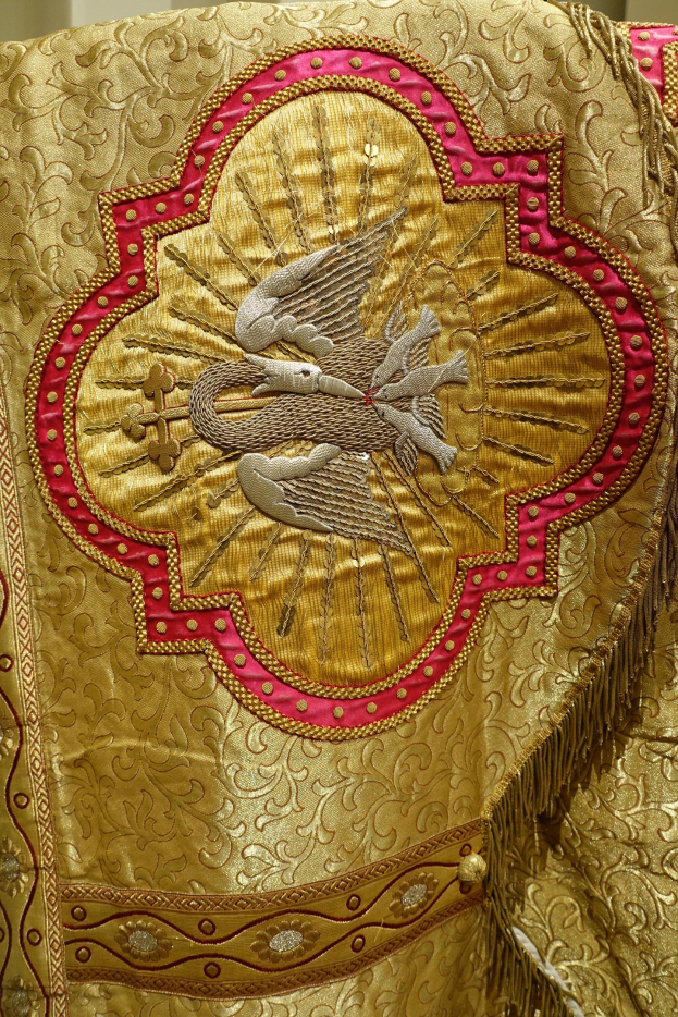 Nahaufnahme eines Priestergewandes mit aufwendiger Gold- und Roterstickerei und luxuriösem, königlichem Design vor einer Wand im Hintergrund.
