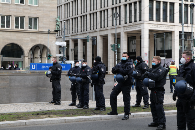 Polizisten in schwarzen Uniformen und Masken stehen vor einem Gebäude mit Glasfenstern und Säulen in Berlin, Deutschland, einige halten Helme.