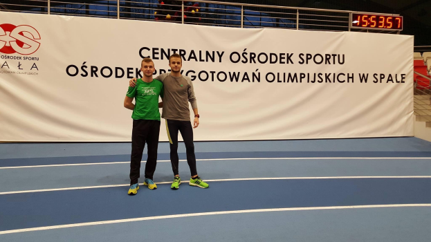 Zwei Männer auf einem Tennisplatz während der Olympischen Spiele 2019, mit einem Banner "Olympische Spiele 2019 - Ostrodek vs Spale" im Hintergrund.
