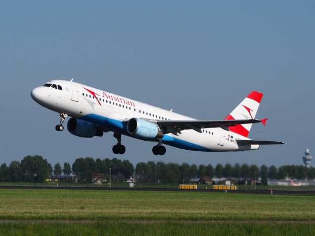 Ein Airbus A320-200 der Austrian Airlines beim Start vom Frankfurt Airport mit Grünflächen, Gebäuden und einer Kontrollturm im Hintergrund.