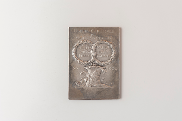 Eine silberne Plakette an einer weißen Wand mit dem Text "Union Centrale" und einem detaillierten Design.